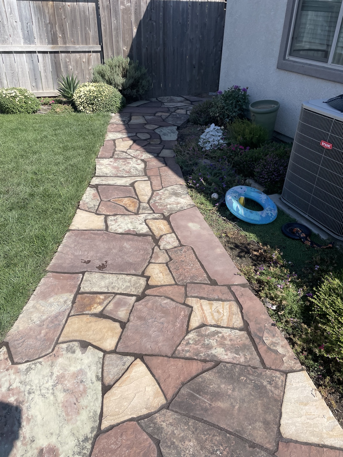 Multicolored natural flagstone walkway beside a lawn and garden