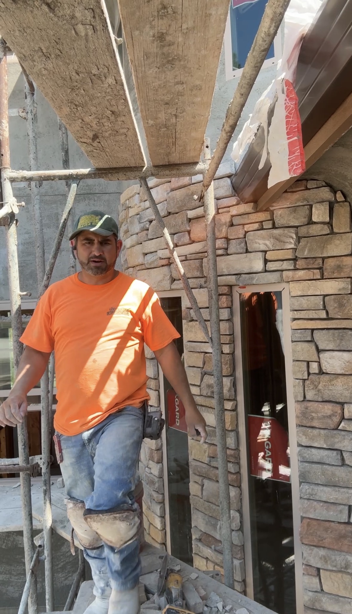 Rodolfo Loza Flores on a stone masonry job site, beside a stone-clad house facade